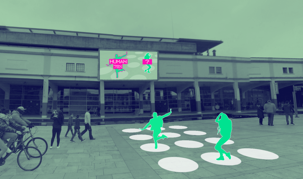 A picture of the large digital screen outside We The Curious. There are people walking through the square. There are two bright green silhouettes of people standing on top of white dots. The screen is showing an image of the green silhouettes with a bright pink text box. 